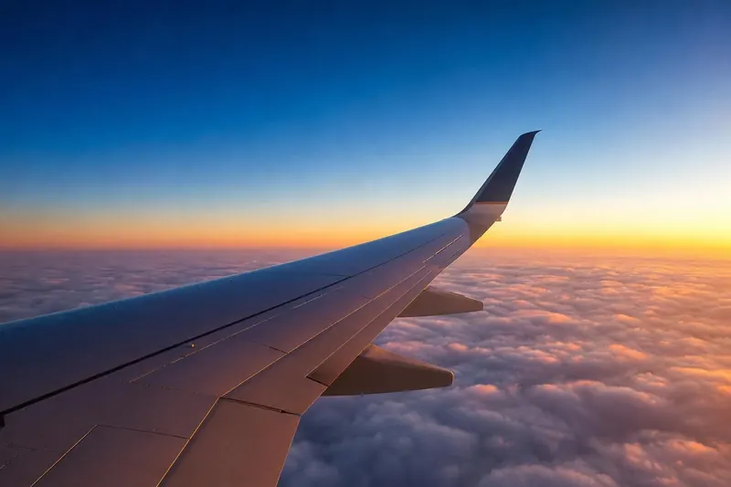 Aircraft wing above the clouds at sunrise — flight booking engine module